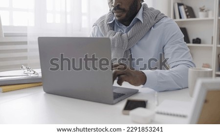 An African American man is working on his laptop, typing an article while sitting in his cozy home office