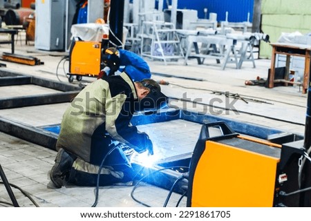 An electric welder works at an industrial enterprise. The process of welding a metal structure from a metal profile. Unrecognizable person. Foreground Royalty-Free Stock Photo #2291861705