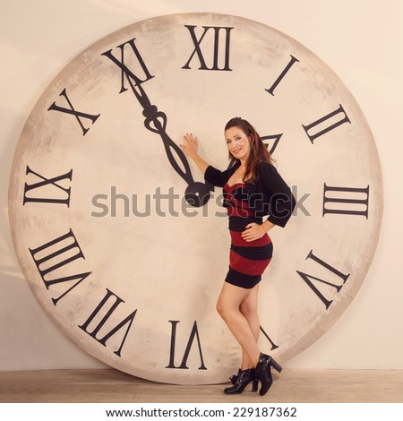 Woman standing near the clock. Arrows show the big clock time. Woman student or office worker. The clock at five minutes to two. Time to take a break for lunch and rest. Two o'clock