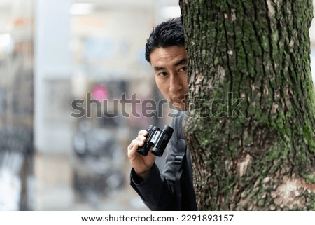 A man hiding in a tree and keeping a lookout with binoculars in the city. Royalty-Free Stock Photo #2291893157
