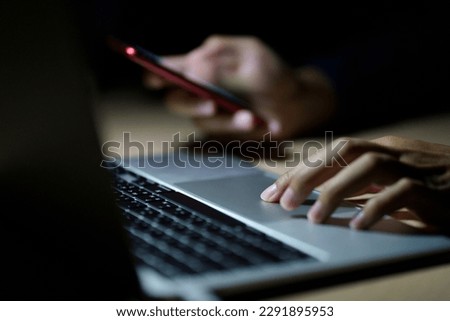 Business man using smart phone, tablet in Dark room. hand holding smart phone , tablet. lap top in front of him.	
