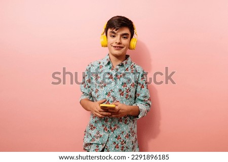 Young guy using smartphone and yellow headphones in studio on pink background.