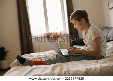 Little cute boy with laptop watching cartoons in bed at home in bedroom