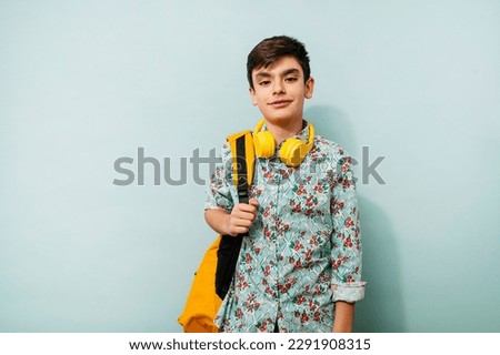 Young guy with yellow headphones and backpack in studio on blue background.