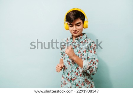 Young guy using yellow headphones in studio on blue background.