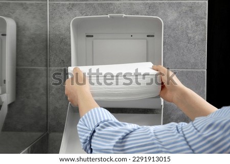 Woman putting new fresh paper towels into dispenser in bathroom, closeup Royalty-Free Stock Photo #2291913015