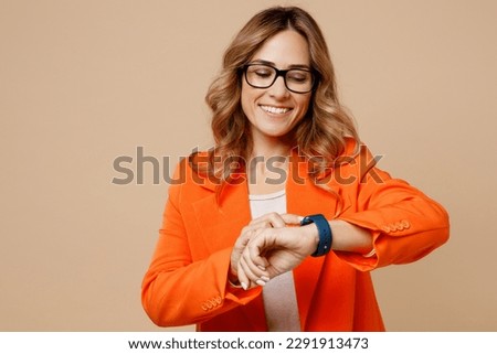 Young smiling happy fun successful employee business woman corporate lawyer 30s wear classic formal orange suit glasses smart watch check time work in office isolated on plain beige background studio Royalty-Free Stock Photo #2291913473