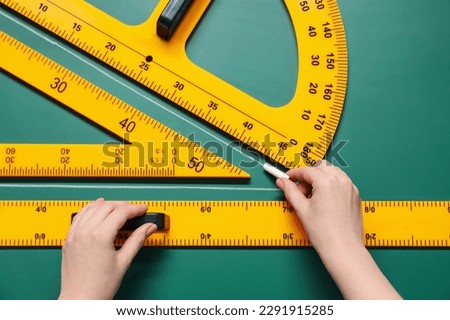 Woman drawing with chalk, ruler, triangle and protractor on green board, closeup