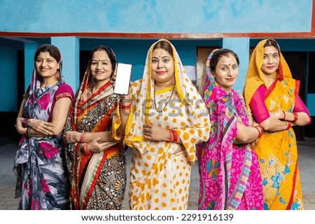 Group of happy young traditional indian women housewives wearing colorful sari showing smart phone with blank display screen to put advertisement, Rural india. women empowerment. Royalty-Free Stock Photo #2291916139