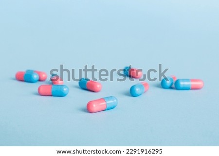 Heap of pink and blue pills on colored background. Tablets scattered on a table. Pile of red soft gelatin capsule. Vitamins and dietary supplements concept.