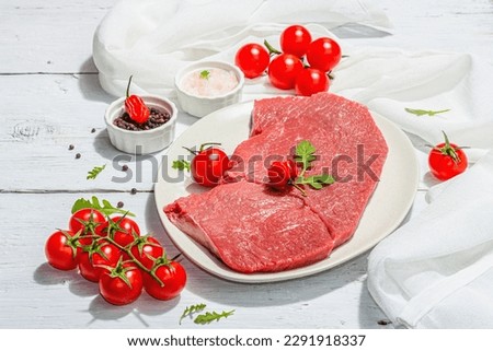 Raw veal steak with spices and cherry tomatoes. A trendy hard light, dark shadow, white wooden background, flat lay, copy space