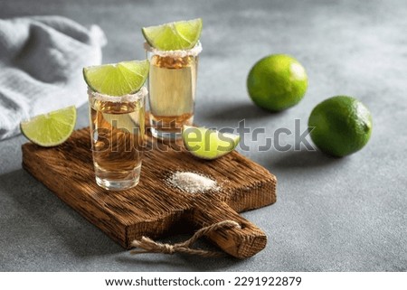 Mexican gold tequila in a shot glass with lime and pink salt on a wooden board, gray concrete background. Side view, selective focus. Royalty-Free Stock Photo #2291922879