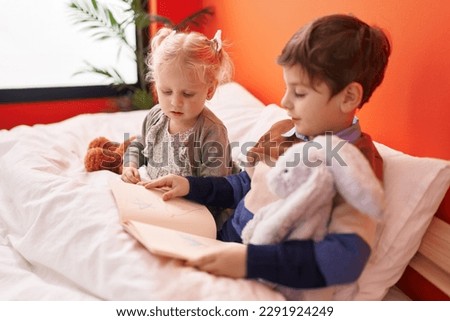 Adorable boy and girl reading book sitting on bed at bedroom