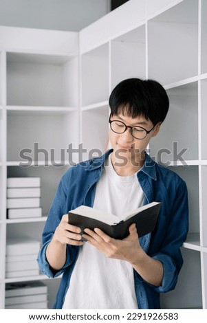 confident male student holding a book and smiling at the camera library bookshelf on background concept of learning and education