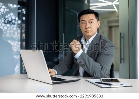 Serious thinking asian businessman working inside office sitting at table with laptop, boss making important financial decision, asian mature man in business suit at workplace. Royalty-Free Stock Photo #2291935333