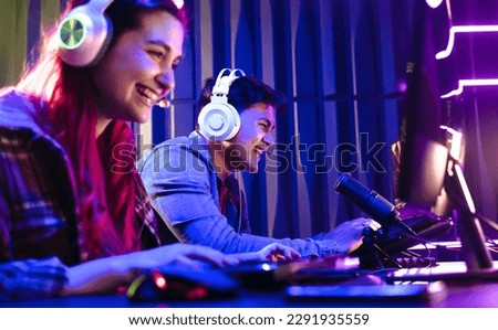 Two young gamers enjoying themselves as they engage in a fun online video game contest. Happy man and woman live streaming their play against each other on a multi monitor setup.