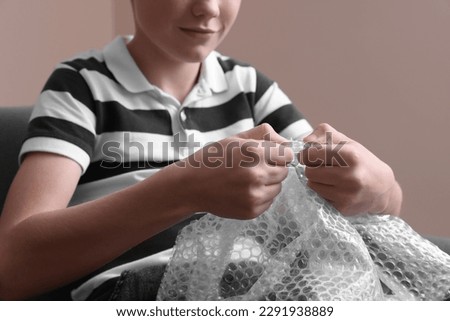 Boy popping bubble wrap indoors, closeup. Stress relief