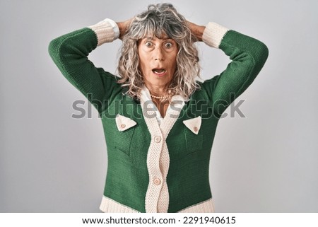 Middle age woman standing over white background crazy and scared with hands on head, afraid and surprised of shock with open mouth 