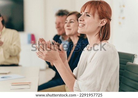 Office Applause Celebration - A group of casually dressed colleagues applauds at the office desk, featuring a young red-haired woman in the foreground and two senior colleagues in the background