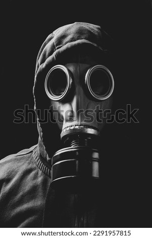 A man in a hood and in a gas mask in clouds of smoke around. Royalty-Free Stock Photo #2291957815