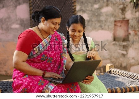 Happy Indian village family of single mother and daughter sitting using the laptop sitting outside the house Royalty-Free Stock Photo #2291957917