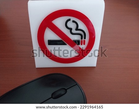 An acrylic sign with a "No Smoking" symbol is placed on a hotel table. A black mouse can be seen next to it. 