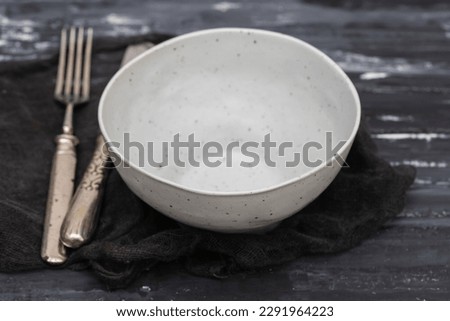 gray ceramics bowl with fork and knife on dark background