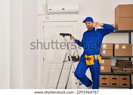 Young hispanic man working at renovation with angry face, negative sign showing dislike with thumbs down, rejection concept 
