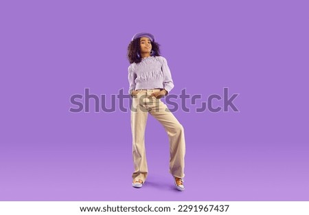 Kid model in stylish fit posing in studio. Full body length beautiful African girl wearing beret hat, blouse and beige wide leg jeans standing on purple background. Clothing, childrens fashion concept