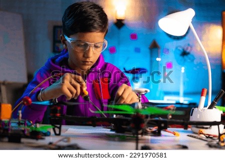 Intelligent serious indian kid busy making drone connections by soldering at home during night - concept of genius, smart kid and innovation. Royalty-Free Stock Photo #2291970581