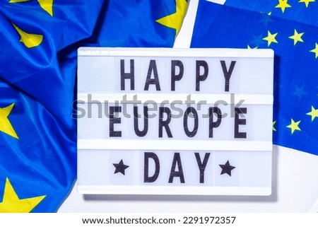 Happy Europe Day simple background, lightbox sign with inscription text Happy Europe Day, flags of Europe (European Union), on white background top view flat lay copy space