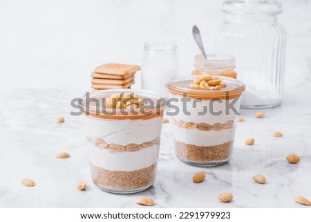 Cheesecake in a jar. Layers of grinded cookies, caramel, peanuts and  cream cheese. Covered in caramel and decorated with peanuts. Selective focus. Macro shot.
