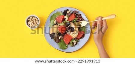 Woman eating tasty grapefruit salad with cashew on yellow background, top view