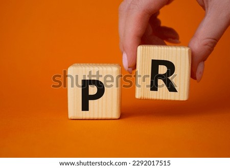 PR - Public Relations symbol. Concept word PR on wooden cubes. Businessman hand. Beautiful orange background. Business and PR concept. Copy space.