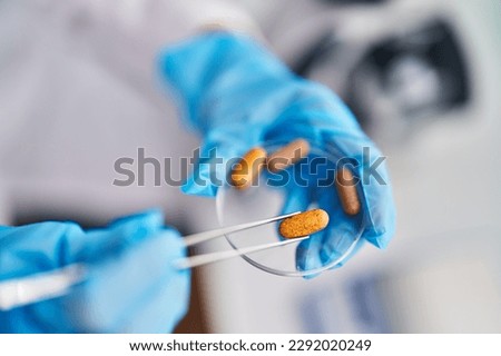 Middle age woman scientist holding pill with tweezers at laboratory Royalty-Free Stock Photo #2292020249
