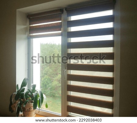 Double roller blinds closeup on the window in the interior. Dual roller shades beige color close-up. Zebra blinds. Royalty-Free Stock Photo #2292038403