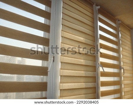 Double roller blinds closeup on the window in the interior. Dual roller shades beige color close-up. Zebra blinds. Duo system day and night. Royalty-Free Stock Photo #2292038405