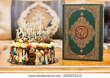 Birthday layer cake decorated with chocolate pieces with happy birthday text with a muslim book with Arabic calligraphy Quran - translation : the noble book of Muslims on wood table