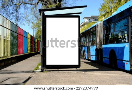 bus shelter at bus stop. white poster and commercial ad space display lightbox. base for mockup. outdoors image. blank ad panel. glass design. urban street setting. green background with spring trees Royalty-Free Stock Photo #2292074999
