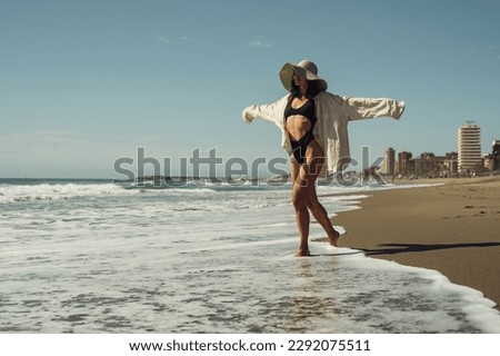 a beautiful girl in a black swimsuit shirt and a straw hat walks