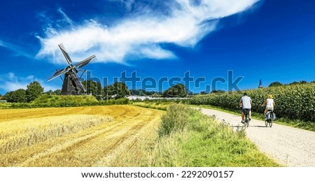 Beautiful dutch bike path, cyclists couple,  scenic limburg maas landscape with windmill (Molen de grauwe beer), blue sunny summer sky - Beesel, Netherlands Royalty-Free Stock Photo #2292090157