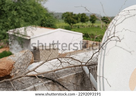 a mix of things in one picture including a farm, farm house, dish antenna, rock and thorns to stop monkeys to climb into the house in a village area