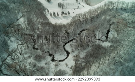 An aerial drone shot of a creek running through a forest during a winter sunrise