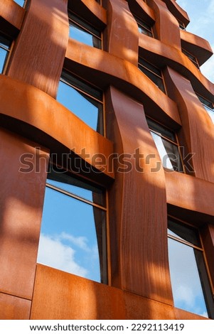 The brown facade of a stylish business building with modern architecture with a grid pattern against a blue sky.