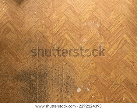 Polyvinyl chloride (PVC) flooring with many dirt spots from renovation. White wall paint blotted on the floor. Cheap material with a wooden look. Abstract background with an empty copy space.