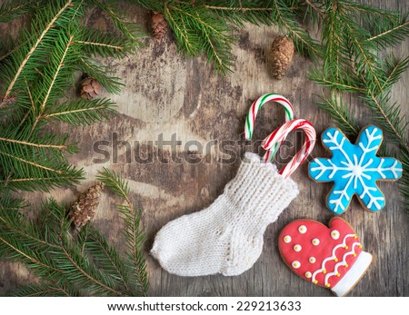 Homemade christmas gingerbreads painted as a red mitten and blue snowflake and small knitted sock with candy canes on the wooden background with fir branches. Selective focus and place for text. Toned