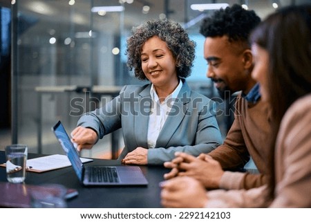Smiling financial consultant and African American couple analyzing their investments on laptop in the office. Royalty-Free Stock Photo #2292142103