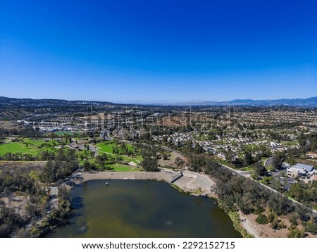 an aerial shot of a gorgeous summer landscape at Laguna Niguel Regional Park with a lake surrounded by mountains covered in yellow flowers, lush green trees and homes with blue sky Laguna Niguel Royalty-Free Stock Photo #2292152715