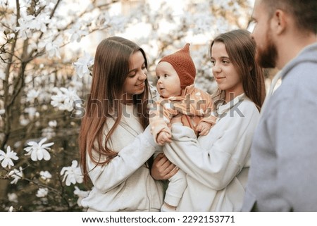 A little child in the arms of twin sisters and with her father is relaxing in the blooming garden. Lifestyle. Family concept. Father and Daughter.  