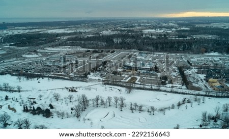 An aerial view of a snow-covered golf course surrounded by a town and forest in the winter